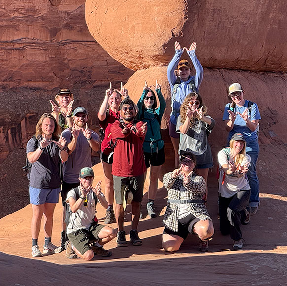 group of people posing in front of a formation of red rocks