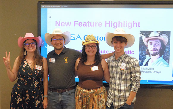 small group of people standing by a screen with the photo of another person on it