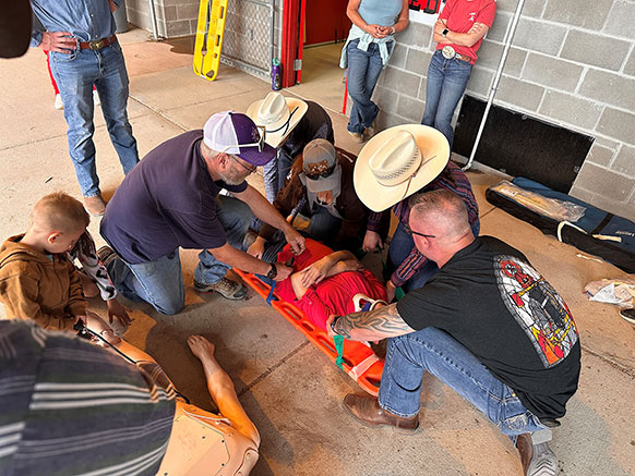 row of people in cowboy clothing standing by a fence at an arena