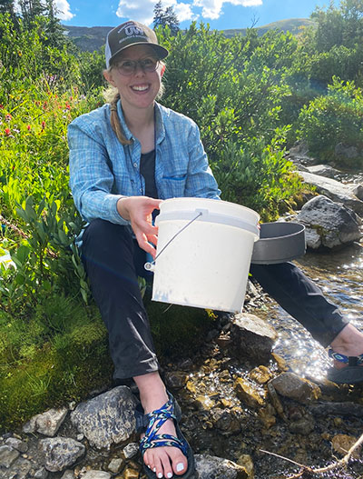 woman sitting beside a stream holding a bucket