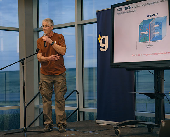 man speaking with a screen display behind him