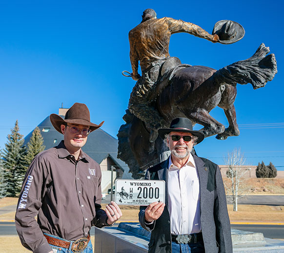 two men holding a license plate in front of a statue