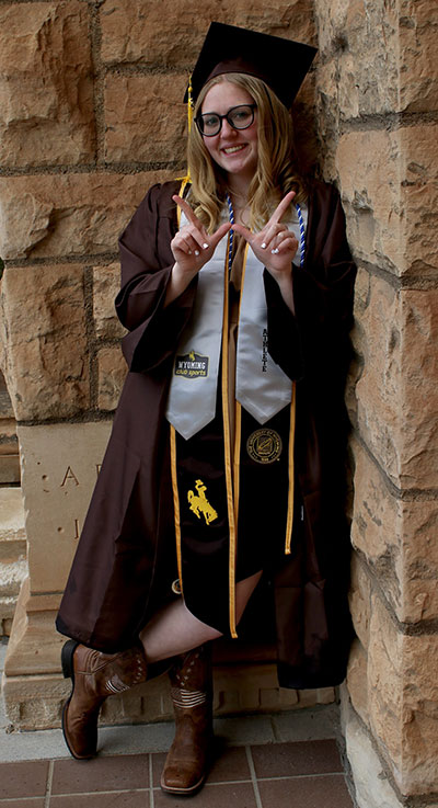 woman in cap and gown leaning against a building