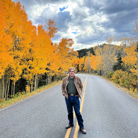 man standing in the middle of a road with golden autumn trees lining it.