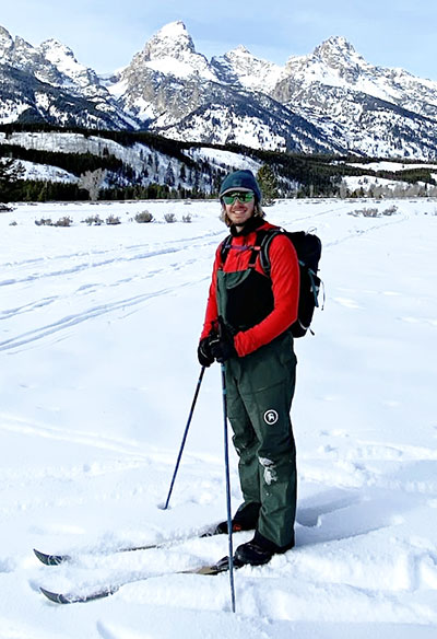 man standing in the snow on skis with mountains behind him