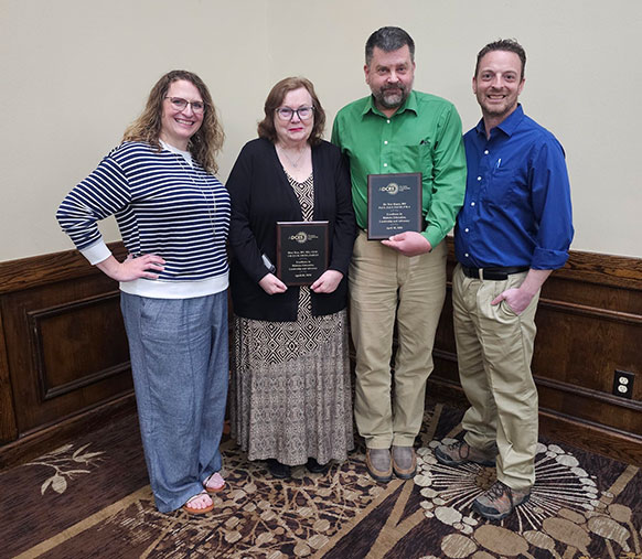 four people posing together with two of them holding awards