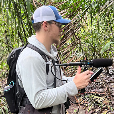 man in a tropical forest holding a large microphone