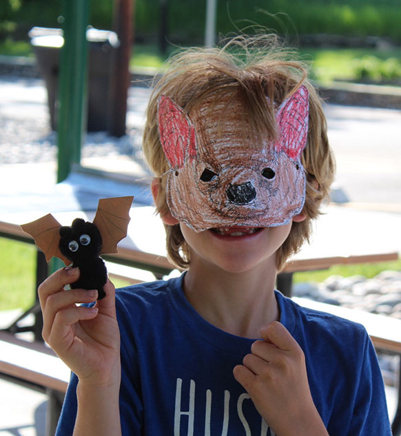 child wearing crayoned bat mask and holding up a small bat toy