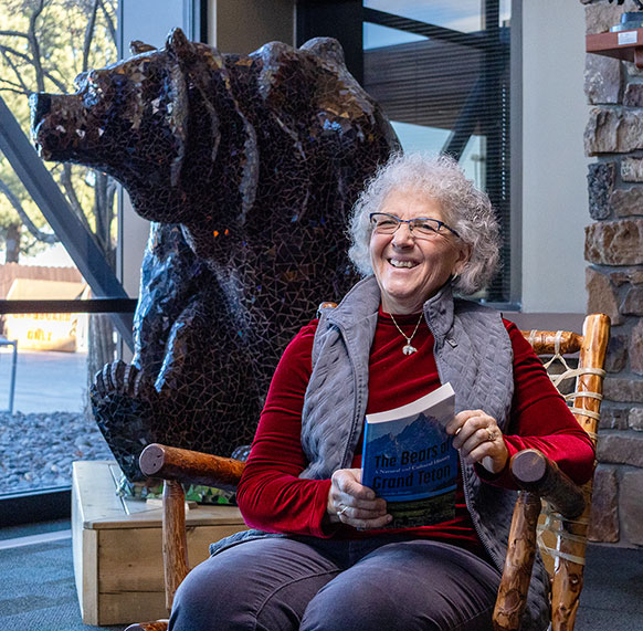 woman sitting holding a book with a bear statue behind her