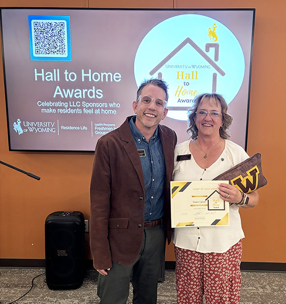 man and woman in front of a screen, with the woman holding awards