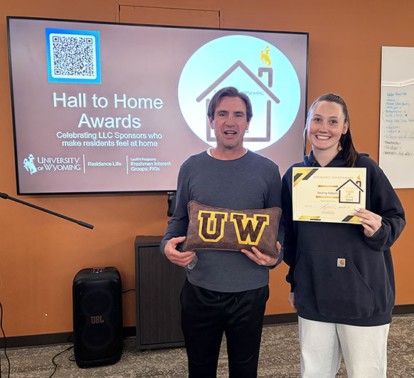 man and woman in front of a screen, posing with awards
