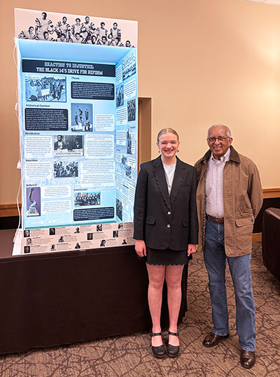 girl and man posing with a poster display