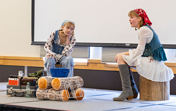 two girls in historical costumes performing on a small stage