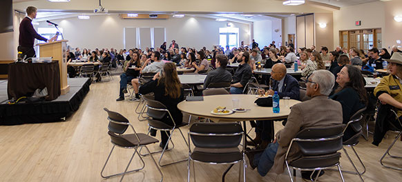 man at a podium speaking to many people at tables