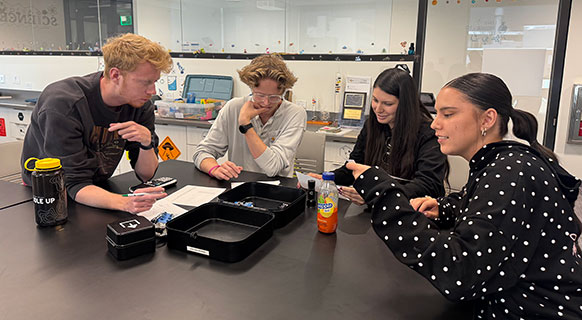 four people seated at a table examining the contents of a box