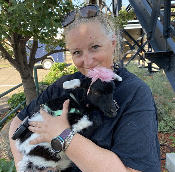 woman holding a small goat, which is wearing a pink headband and fabric flower