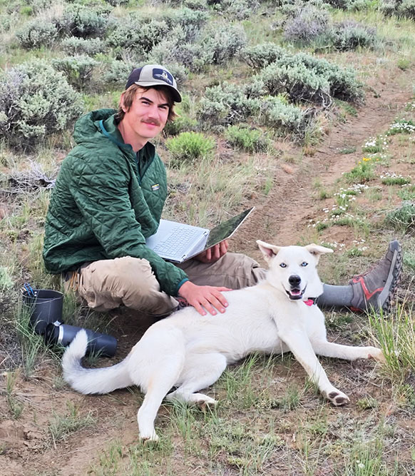 man and a dog sitting on a dirt track in the sagebrush