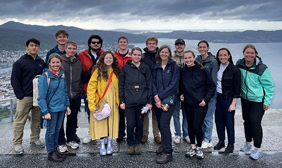 group of people posing beside a body of water with dark clouds and mountains in the distance