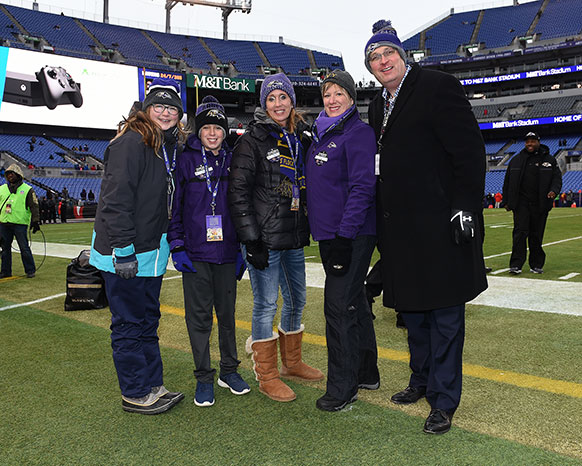 A family of five people in Balitmore Ravens football clothing standing on a football field