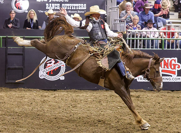 man riding a bucking horse in an arena