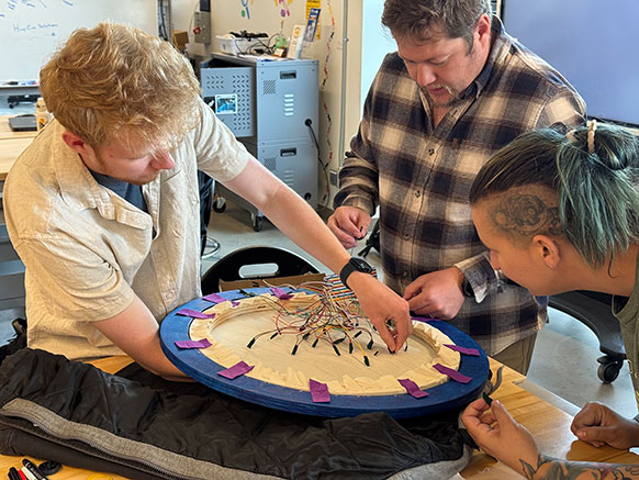 three people moving wires on a circular object