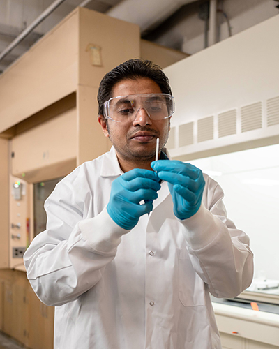 A University of Wyoming professor holds a flu test nasal swab while wearing gloves and a lab coat.