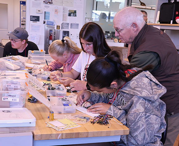 man helping students at a large table full of equipment