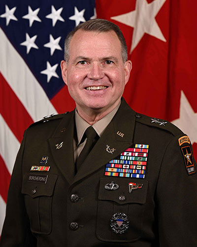 man in a military uniform standing in front of a U.S. flag