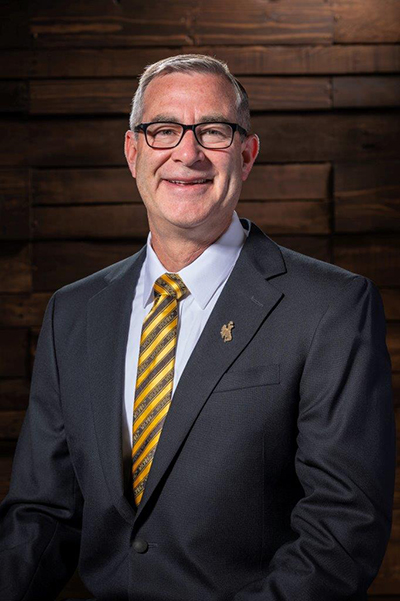 Shane Reeves stands in front of a wooden background.