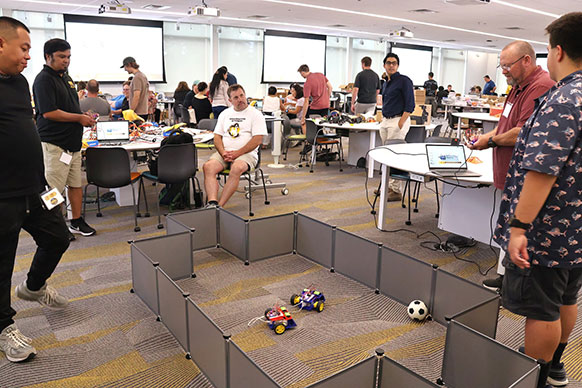 people in a large room watching a pen with small robots in it