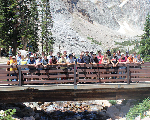 large group of teenagers on a footbridge with a rocky mountain slope behind them