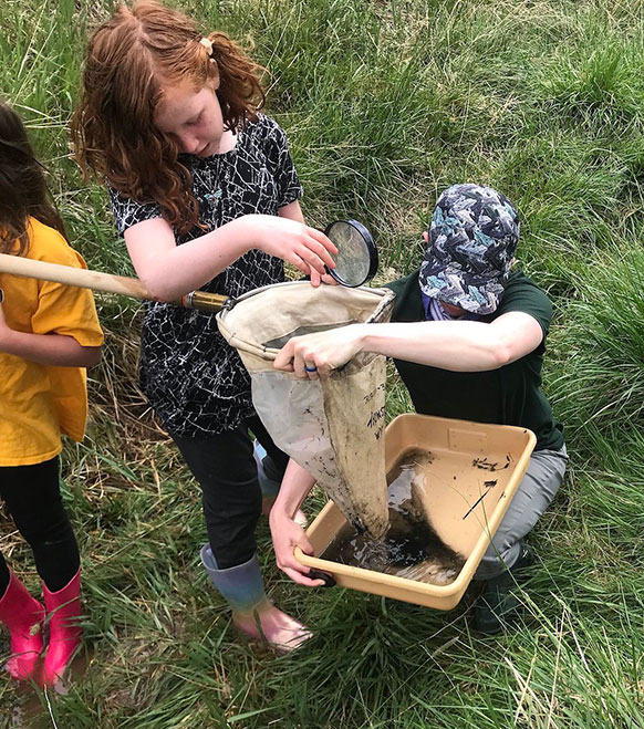 woman helping kids shake a net into a tub of water