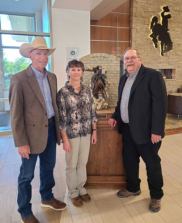 three people standing around scupture of a horse breaking through a wall