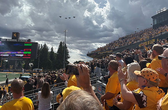 fans in stadium looking up at jets flying overhead