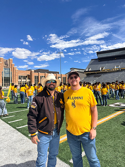 A man wearing a University of Wyoming jacket and a cowboy hat stands on the football field with a man wearing a University of Wyoming shirt.