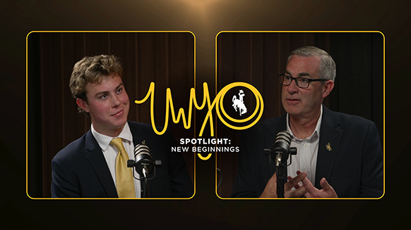 A young man in a suit smiles on the left side, and an older man in a suit speaks on the right side..