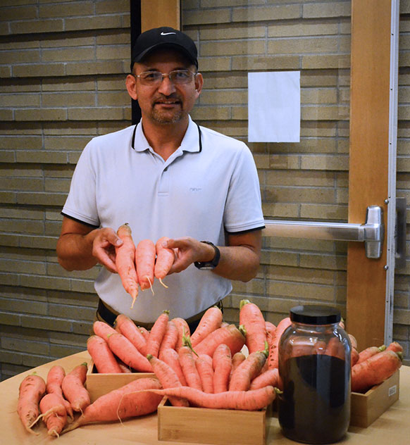 man standing behind a table with lots of large carrots