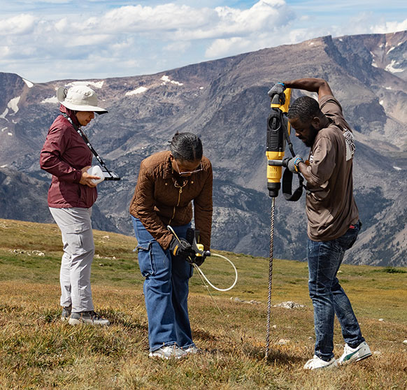 three people in the mountains drilling out samples from the ground