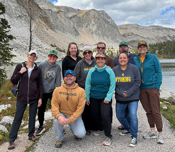 group of people posing with a lake and mountains in the background