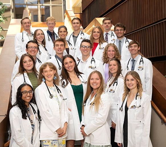 group of people in white coats and stethosopes posing on a staircase