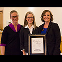 Three women smile broadly as the center hold award.