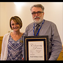 tall man with great hair, mustache and beard holding award with shorter woman beside him.
