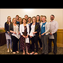 12 students standing together in somewhat of a huddle.