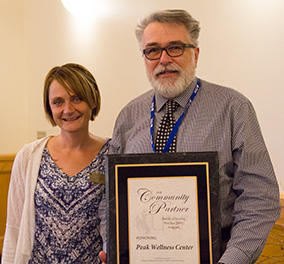 woman accompanies may with beard holding award plaque