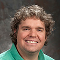 smiling young man in green shirt and curly brown-gray hair