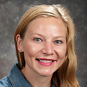 Smiling yung woman with blond hair pulled around her to gall down her left shoulder