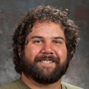young man with dark curly hair and full beard and mustache