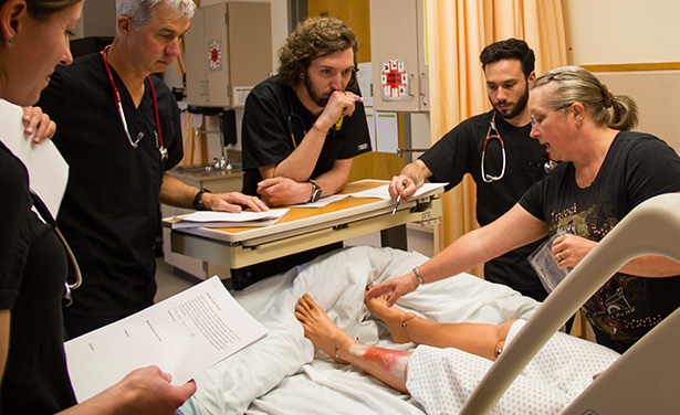 Four students in black scrubs listen to faculty pointing out something on the feet of the maniken."