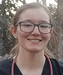 student in nursing gear standing outside with wooded background