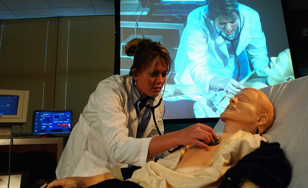 Student checks heartbeat of manikin with image blown up on screen for entire class to view. 